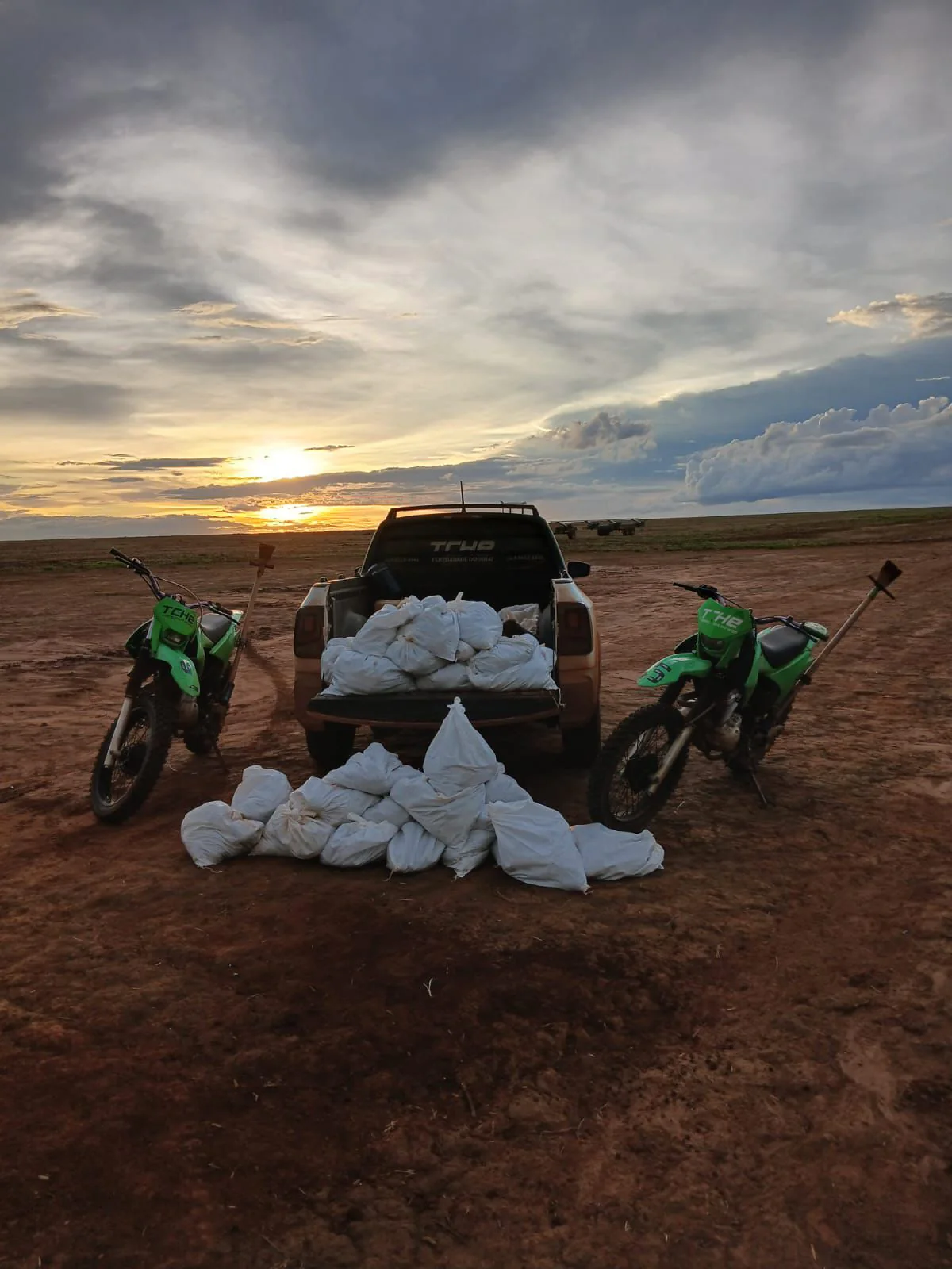 Veículo, motocicletas e materiais da Tchê organizados em área de campo